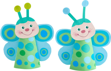 Zwei Papierbasteleien in Form von Schmetterlingen, jeweils mit lächelndem Gesicht, blauen Flügeln mit grünen und blauen Punkten und grünen kegelförmigen Körpern, die mit blauen und grünen Kreisen verziert sind.