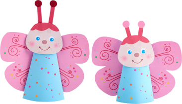 Zwei Papierbasteleien in Form von Schmetterlingen mit rosa Flügeln, blauen kegelförmigen Körpern, roten Fühlern und lächelnden Gesichtern. Die Flügel haben gewirbelte und gepunktete Muster in verschiedenen Farben.