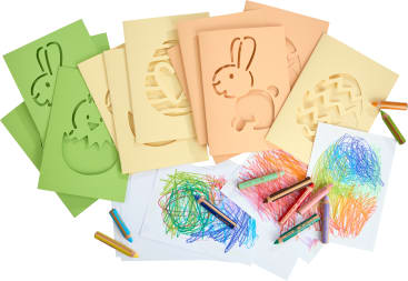Mehrere farbige Papierschablonen von Hasen und Eiern sind mit Buntstiften und Papierblättern ausgelegt, die bunte Kritzeleien zeigen, was auf eine künstlerische Tätigkeit der Kinder hindeutet.
