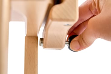 Nahaufnahme einer Hand, die einen schwarzen Knopf an einem hölzernen Möbelstück verstellt und möglicherweise eine Verbindung zwischen zwei Holzteilen festzieht oder lockert.