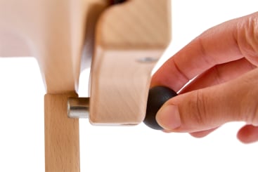Eine Hand stellt einen runden schwarzen Knopf ein, der mit einer Metallstange an einer leichten Holzstruktur befestigt ist. Der Hintergrund ist weiß.