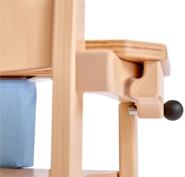 Nahaufnahme eines hellen Holzstuhls mit einer blauen Stofftasche unter der Sitzfläche und einem runden schwarzen Knopf an der Seite.