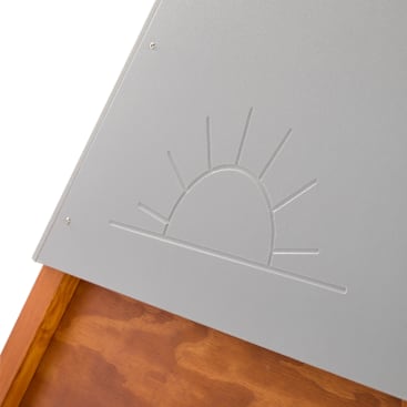 Nahaufnahme einer grauen Metallplatte mit einem eingravierten Sonnenaufgangsmotiv, das über einem Holzteil mit sichtbaren Schrauben an den Ecken angebracht ist.