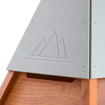 Nahaufnahme einer grauen Metalltafel mit dem eingravierten Umriss von drei Berggipfeln über einer horizontalen Linie, die an einer Holzkonstruktion befestigt ist.