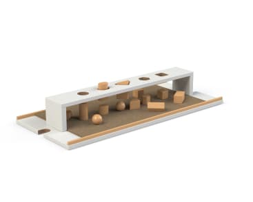 Ein weißer rechteckiger Formensortierer mit einer Reihe von Löchern für verschiedene Formen, der auf einer braunen Fläche steht. Verschiedene geometrische Holzteile, wie Kugeln, Würfel und Zylinder, sind darunter und darum herum verstreut.
