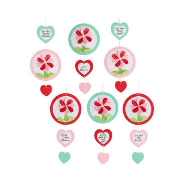 Eine Hängedekoration mit kreisförmigen Blumenmotiven und herzförmigen Anhängern. Die Anhänger tragen deutsche Botschaften wie "Für die beste Mama", "Für Mutti" und "Alles Liebe, Mama". Die Farben sind rosa, rot, grün und weiß.