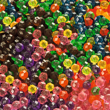 Eine Nahaufnahme von vielen bunten, facettierten Kunststoffperlen in verschiedenen Farben, darunter grün, gelb, rosa, lila, rot und schwarz, die dicht an dicht liegen und das gesamte Bild bedecken.