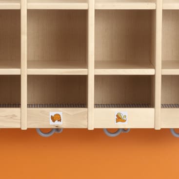 Ein Holzregal mit vier Fächern, von denen zwei auf der Vorderseite mit Aufklebern versehen sind: einer mit einer Schildkröte und einer mit einem Vogel. Das Regal ist über einer orangefarbenen Wand angebracht.