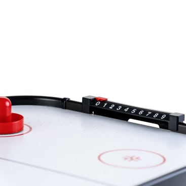 Nahaufnahme eines Tisch-Airhockeyspiels mit einem roten Schläger, einem Teil der weißen Spielfläche mit roten Markierungen und einem schwarzen manuellen Punktezähler mit den Ziffern 0 bis 9.