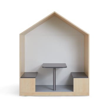 Eine hölzerne Kabine in Form eines Hausrahmens mit zwei eingebauten Bänken, die sich gegenüberstehen, und einem rechteckigen schwarzen Tisch in der Mitte, der vor einem schlichten weißen Hintergrund steht.