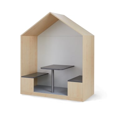 Eine hölzerne Kabine in Form eines Hauses mit einem Spitzdach, mit zwei eingebauten Bänken und einem quadratischen Tisch in der Mitte. Die Oberflächen von Tisch und Bänken sind dunkelgrau.
