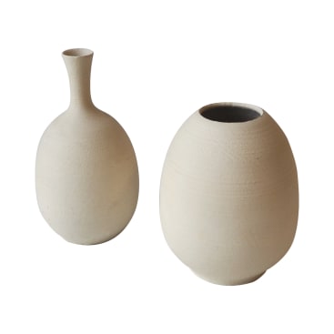 Zwei beigefarbene Keramikvasen sind vor einem weißen Hintergrund abgebildet. Die Vase auf der linken Seite hat einen schmalen Hals und einen abgerundeten Boden, während die Vase auf der rechten Seite runder ist und eine breite Öffnung hat. Beide haben eine glatte, matte Oberfläche.