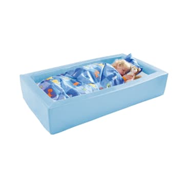 Ein kleines Kind schläft auf der Seite in einem hellblauen Schaumstoffbett, zugedeckt mit einer blauen Decke mit bunten Tiermustern und mit einem passenden Kissen. Der Hintergrund ist einfarbig weiß.