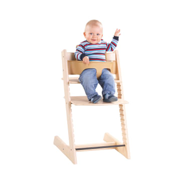 Ein Baby in einem gestreiften Pullover und Jeans sitzt in einem hölzernen Hochstuhl, hebt eine Hand und lächelt. Der Hintergrund ist einfarbig weiß.