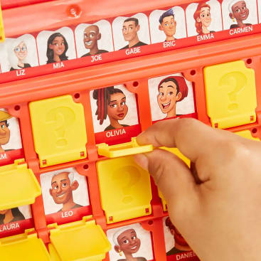 Eine Hand hebt eine gelbe Klappe auf einem Guess Who?-Spielbrett an und enthüllt eine Karte mit einer Figur namens Olivia. Weitere Charakterkarten mit Namen und illustrierten Gesichtern sind rund um das Spielbrett zu sehen.