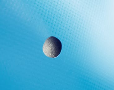 Eine Nahaufnahme eines kleinen, runden Lochs in einer strukturierten hellblauen Oberfläche. Das Loch offenbart ein dunkles Inneres und wirft einen Schatten auf das umgebende Material.
