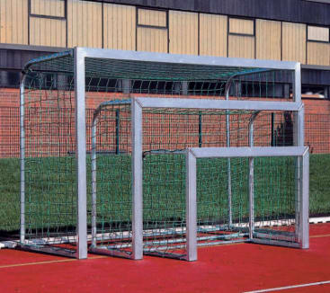 Drei unterschiedlich große Fußballtore sind auf einem roten Sportplatz ineinander verschachtelt, mit einem grünen Rasen und einem Gebäude mit Ziegelwänden und beigen Platten im Hintergrund.