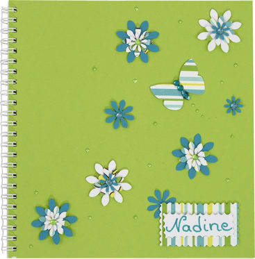 Ein grünes Notizbuch mit Spiralbindung, verziert mit blauen und weißen Papierblumen, einem gestreiften Schmetterling und einem Etikett mit Wellenschliff und dem Namen Nadine in grüner Schrift.