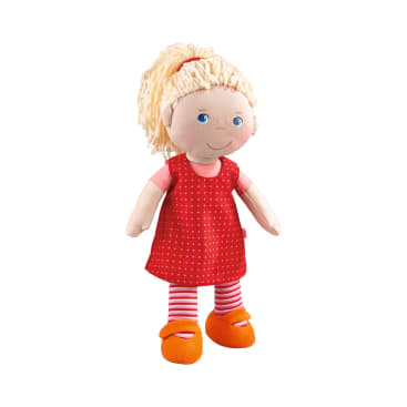 Eine weiche Puppe mit blondem Garnhaar in einem Pferdeschwanz, die ein rotes Kleid mit weißen Punkten, rosa und weiß gestreifte Leggings und orangefarbene Schuhe trägt, wird vor einem weißen Hintergrund gezeigt.