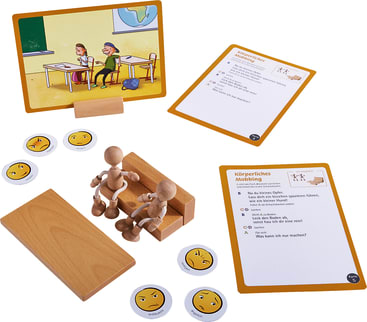 Ein pädagogisches Tischset mit Holzfiguren, illustrierten Karten, runden Emoji-Marken, einer kleinen Bank, einem Schreibtisch und einem Ständer mit einem Bild von Kindern in einem Klassenzimmer. Die Materialien scheinen Mobbing zu thematisieren.