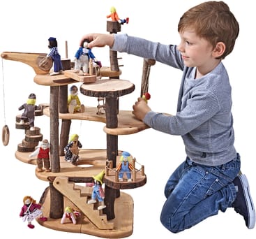 Ein kleiner Junge kniet auf dem Boden und spielt mit einem mehrstöckigen Puppenhaus aus Holz, in dem kleine Holzpuppen auf verschiedenen Ebenen, Treppen und Plattformen stehen.