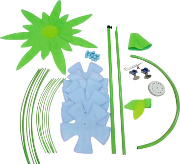 Eine Sammlung von Kunststoff- und Stoffteilen auf weißem Hintergrund, darunter grüne Stäbe, blaue kreuzförmige Teile, runde blaue Kugeln, Blätter und Blütenblätter aus Stoff und kleine Hardwarekomponenten.