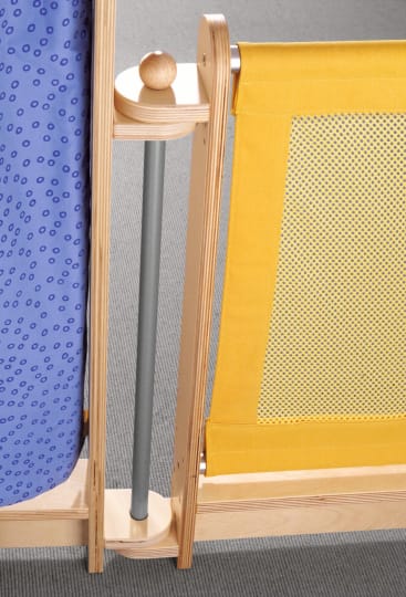 Nahaufnahme eines Holzrahmens mit einem blauen Stoffpaneel auf der linken Seite und einem gelben Netzstoffpaneel auf der rechten Seite, die beide an einer Grundplatte auf einer grauen Teppichfläche befestigt sind.