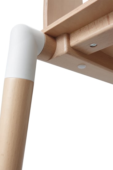 Nahaufnahme eines Tisch- oder Möbelbeins aus Holz mit einer weißen Kunststoffverbindung, die das Bein mit der Tischplatte verbindet. Das Holz hat eine helle Oberfläche und eine sichtbare Maserung, es sind Schrauben und eine runde weiße Abdeckung vorhanden.