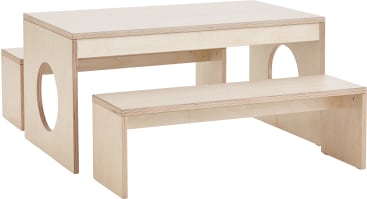 Ein Kindertischset aus hellem Holz mit zwei Bänken. Tisch und Bänke haben schlichte, moderne Linien, und beide Bankseiten sind mit kreisförmigen Ausschnitten versehen. Das Holz hat eine glatte, natürliche Oberfläche.