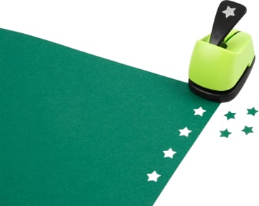 Ein sternförmiger Locher und mehrere ausgestanzte Sternformen befinden sich auf einem Blatt grünen Papiers. Der Locher ist lindgrün und schwarz, und fünf sternförmige Ausstanzungen sind auf der Oberfläche sichtbar.