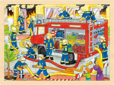 Feuerwehrleute mit gelben Helmen und blauen Uniformen arbeiten um ein Feuerwehrauto herum und ziehen Schläuche und Ausrüstung, während im Hintergrund ein Gebäude brennt. Eine Frau und ein Kind schauen hinter einer Absperrung zu.