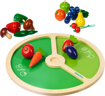 Ein Holzspielzeug mit verschiedenen bemalten Holzfrüchten und -gemüsen, darunter eine Karotte, eine Aubergine, ein Pilz und Weintrauben, die neben und auf einem grünen Tablett angeordnet sind.