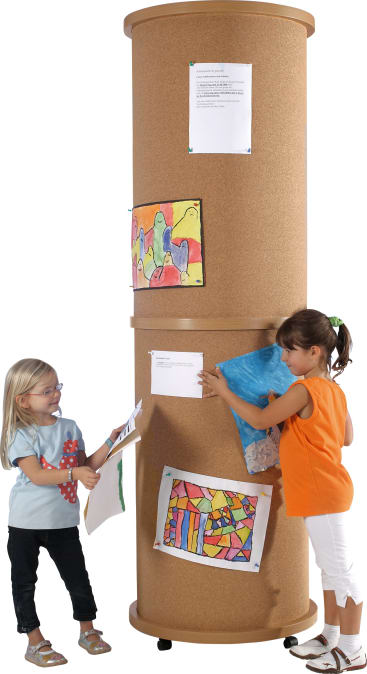 Zwei kleine Kinder stehen neben einer großen zylindrischen Korkwand auf Rädern. Die Mädchen posten und betrachten bunte Kunstwerke und Papiere, die in verschiedenen Höhen an der Tafel befestigt sind.