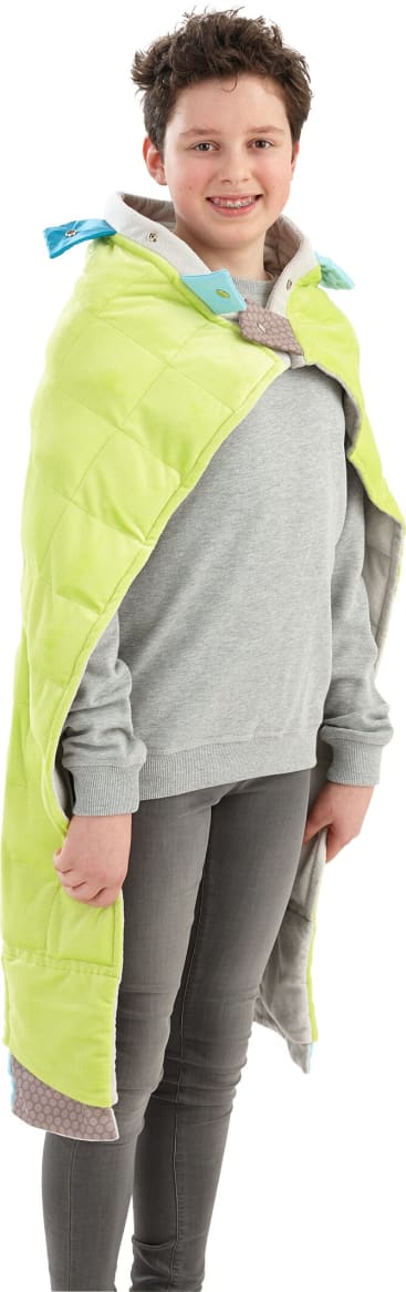Eine Person mit kurzen dunklen Haaren, die einen grauen Pullover und eine graue Hose trägt, steht da und lächelt. Sie hat eine hellgrüne Steppdecke über die Schultern gelegt, die im Nacken verschlossen ist.
