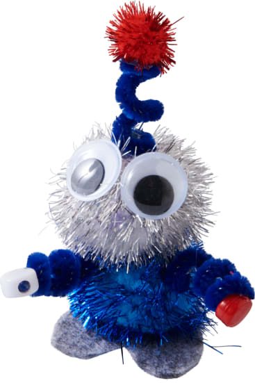 Eine kleine Bastelfigur aus blauem und silbernem Lametta, mit großen Kulleraugen, Pfeifenreinigerarmen, einem roten Bommel an der Spitze und Filzfüßen, die in jeder Hand kleine Plastikgegenstände hält.