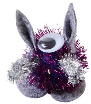 Eine kleine Bastelfigur aus lilafarbenem und silbernem Lametta, grauem Filz, zwei aufrechten Filzohren und einem einzigen großen Plastik-Googly-Auge auf der Spitze.