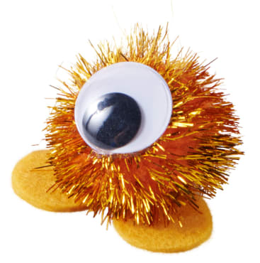 Ein kleines handwerkliches Geschöpf aus orangefarbenem und goldenem Lametta, mit einem großen Kunststoff-Googly-Auge und zwei flachen gelben Filzfüßen, vor einem weißen Hintergrund.