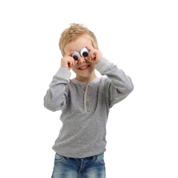 Ein kleines Kind in einem grau gestreiften Hemd und Jeans hält sich große Kulleraugen über die eigenen Augen und lächelt, während es vor einem weißen Hintergrund steht.