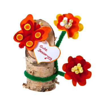 Ein kleiner Birkenstamm ist mit Filzblumen und einem Schmetterling aus Filz verziert. Am Stamm ist ein weißes herzförmiges Schild mit der Aufschrift "Gute Besserung" in Rot angebracht.