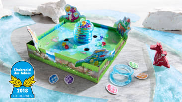 Ein farbenfrohes Kinderbrettspiel mit einem grünen Schachtelboden, einem zentralen Plastikbienenstock, bunten Edelsteinen, Dinosaurierfiguren aus Pappe, Spielplättchen und einem blauen "Kinderspiel des Jahres 2018"-Abzeichen unten links.