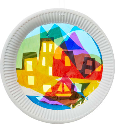 Ein kreisförmiger weißer Pappteller mit ausgeschnittener Mitte, gefüllt mit bunten, durchscheinenden Papierstücken, die so angeordnet sind, dass sie Gebäuden und geometrischen Formen ähneln und einen Buntglaseffekt erzeugen.
