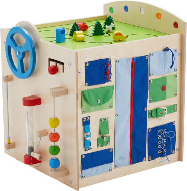 Ein Aktivitätswürfel aus Holz mit einem blauen Lenkrad, Perlen an Stäben, Reißverschlüssen, Knöpfen, Schnürsenkeln und Stoffbeuteln an den Seiten. Auf der Oberseite befindet sich ein Spielbereich mit Spielzeugautos, Bäumen und Gebäuden.