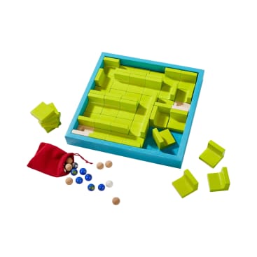 Ein hölzernes Puzzlespiel mit grünen Labyrinthteilen in einem blauen Rahmen, mehrere Teile entfernt und verstreut, zusammen mit Murmeln und einem kleinen roten Beutel auf weißem Hintergrund.