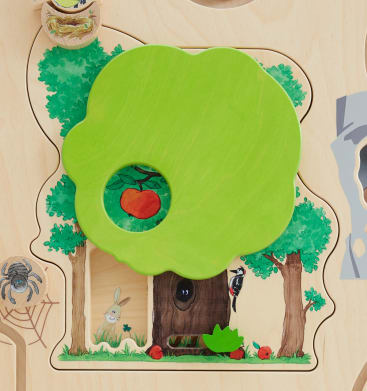Ein Holzpuzzle mit einem großen grünen baumförmigen Teil, das einen kreisförmigen Ausschnitt abdeckt und darunter einen gemalten roten Apfel offenbart. Das Puzzlebrett zeigt Abbildungen von Bäumen, einem Kaninchen, einer Spinne und einem Specht.