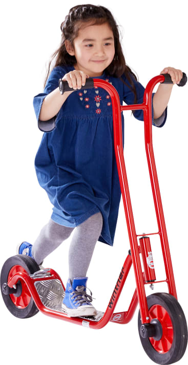 Ein junges Mädchen in einem blauen Kleid, grauen Leggings und blauen Turnschuhen fährt auf einem roten Motorroller. Sie hält den Lenker mit beiden Händen fest und lächelt leicht. Der Hintergrund ist weiß.