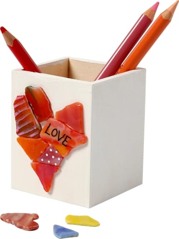 Ein weißer Bleistifthalter aus Holz, verziert mit bunten, zerbrochenen Keramikstücken, die eine Herzform und das Wort LOVE bilden. Drei Buntstifte befinden sich im Inneren und drei weitere Keramikstücke liegen vor dem Halter.