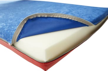 Nahaufnahme einer Schaumstoffmatratze mit einem blauen Stoffbezug, der teilweise geöffnet wurde, um die weiße Schaumstoffpolsterung im Inneren und eine rote Unterschicht zu enthüllen.