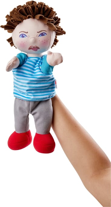 Eine Hand hält eine Stoffpuppe mit braunem Filzhaar, einem wütenden Gesichtsausdruck, einem blau-weiß gestreiften Hemd, einer grauen Hose und roten Schuhen. Die Arme der Puppe sind erhoben. Der Hintergrund ist weiß.