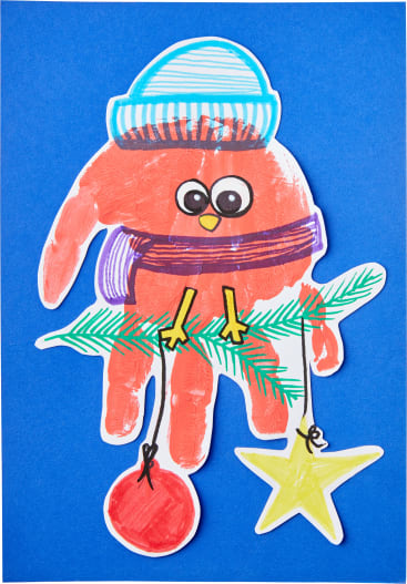 Ein aus einem roten Handabdruck ausgeschnittener Vogel mit gezeichneten Details, der einen blauen Hut und einen lila Schal trägt und auf einem grünen Zweig mit einem roten Ornament und einem gelben Stern sitzt. Der Hintergrund ist blau.
