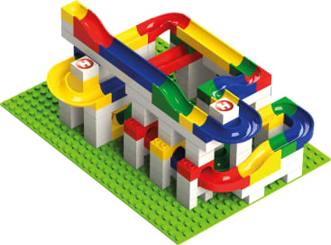 Auf einer grünen Grundplatte ist eine bunte LEGO Murmelbahn mit roten, gelben, blauen und grünen Bahnen aufgebaut, die sich in Schleifen und Kurven um weiße Ziegelstützen winden.